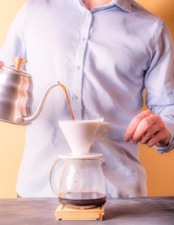 Person concentrating on manually brewing coffee with a pour-over filter setup, Vertical aspect