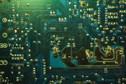 Close-up of green lighted electronic computer circuit board with silver solder points and lines,