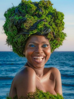 Woman with bright smile wearing a lush greenery headdress against an ocean background, moss growing