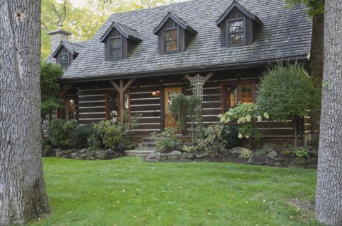 White chinked log cabin home facade with grey weathered cedar shingles roof, three dormer windows