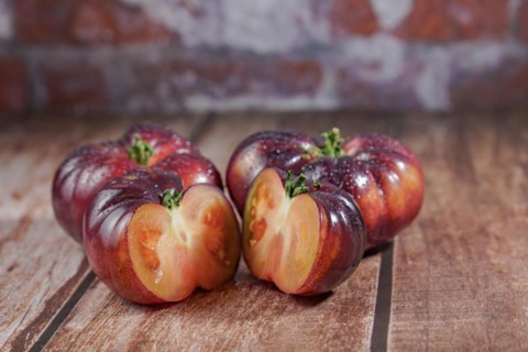 Group of tasty fresh tomatoes of the blue variety with a halved tomato dipped in water drops on a