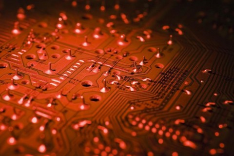 Close-up of red lighted electronic computer circuit board with silver solder points and lines,