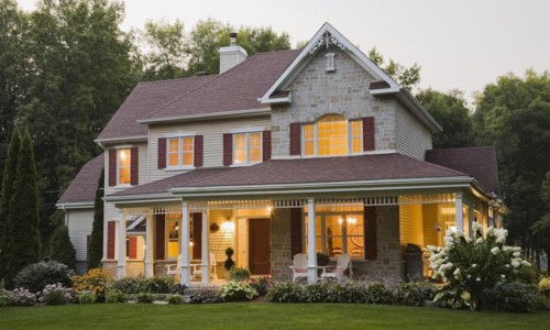 Large illuminated two story beige and tan cut stone home exterior with white and red trim, multiple