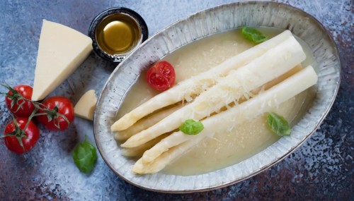 Creamy white asparagus soup in an oval ceramic bowl decorated with basil and tomato, cooked white
