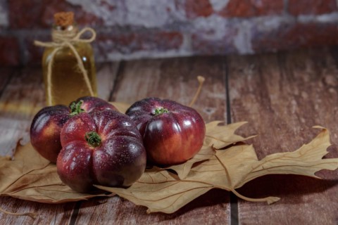 Group of tasty fresh tomatoes of the blue variety with drops of water on dry leaves next to ears of