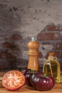 Group of tasty fresh tomatoes of the blue variety together with wooden tongs, a glass bottle of