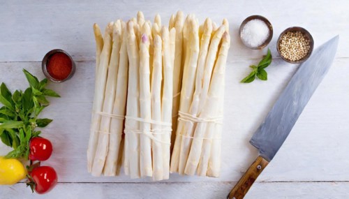 Fresh asparagus arranged on a wooden board next to kitchen utensils and fresh herbs, KI generated,