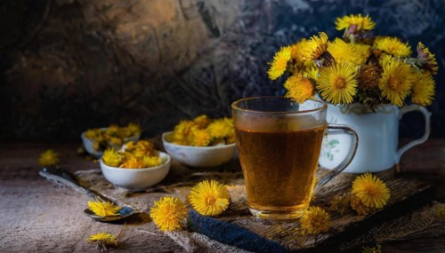Cosy tea set-up with coltsfoot and fresh flowers arranged on a wooden table, coltsfoot tea,