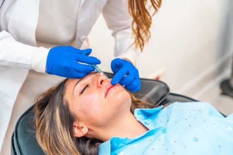 Cosmetologist making botox injection to the face of a caucasian adult woman in a clinic