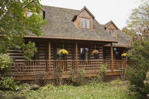 Rustic white chinked two story log home with long veranda and cedar shingles roof covered with