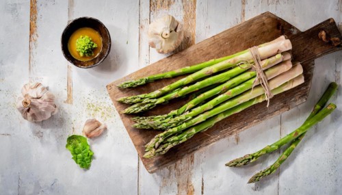 Bundles of asparagus on an old wooden board with garlic and dressing, green asparagus, asparagus