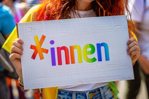 Woman holding up sign with colorful text saying *innen, a suffix used for gender neutral language
