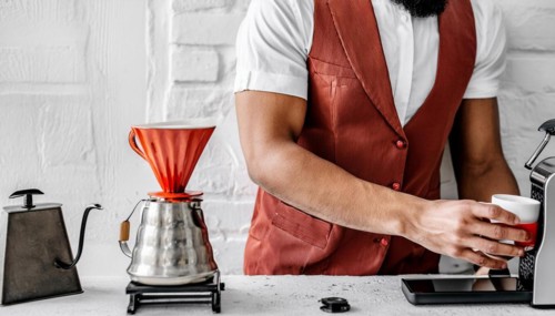 Unrecognizable Barista fashionista in an leather vest and white t-shirt apron brewing pour-over
