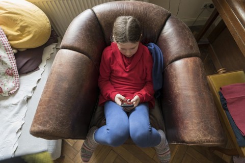 Symbol photo mobile phone, internet, addiction, little girl, 10 years old, sitting in an armchair