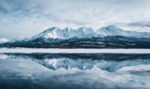 A distant view of snow-capped mountains reflected in the frozen surface of a lake AI generated