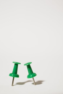 Close-up of two upright green plastic and chrome pushpins on white background, Studio Composition,