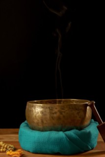 Tibetan singing bowl smoking on green cloth next to a Buddhist japa mala isolated on black