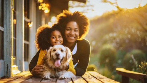 A woman and a child are laying on the ground with a golden retriever. Scene is warm and loving, as