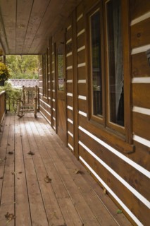 Long old and worn brown stained veranda with pine wood rocking chair on facade of rustic white