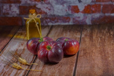 Group of tasty fresh blue tomatoes on a wooden table next to ears of wheat with a bottle of olive