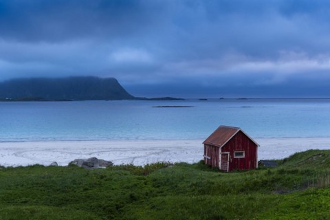 A red wooden hut on the sandy beach of Ramberg (Rambergstranda), sea and mountains. At night at the