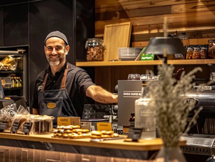 Friendly barista smiling at the camera in a warmly lit coffee shop with a casual ambiance, coffee