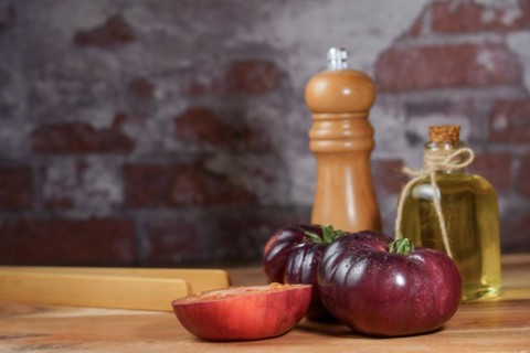 Group of tasty fresh tomatoes of the blue variety together with wooden tongs, a glass bottle of
