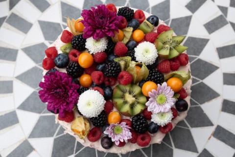 A colourful fruit cake with fresh berries and flowers on a patterned background, Germany, Europe