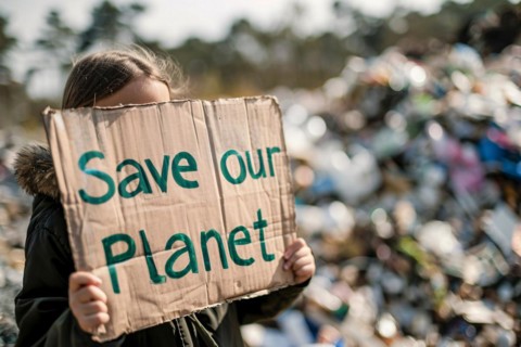 Activist with cardboard sign with text 'Save our planet' in front of blurry mountain of garbage. KI
