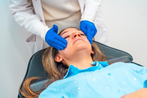 Aesthetic female doctor applying numbing cream on the face of a woman before injecting hyaluronic