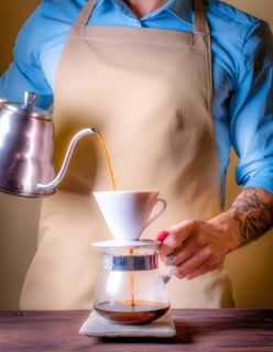 A tattooed arm expertly pours hot water for coffee brewing, highlighting the maker's focus,