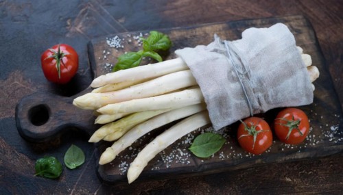 A bunch of asparagus next to ripe cherry tomatoes on a rustic background, bunch of white asparagus