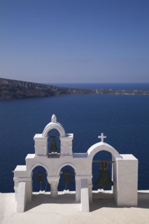 White roughcast cladded arched church bells tower with cross overlooking the Aegean sea, Oia
