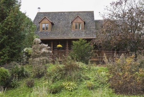 Rustic white chinked two story log home with long veranda and cedar shingles roof covered with