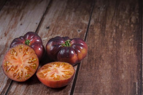 Group of tasty fresh tomatoes of the blue variety with a halved tomato dipped in water drops on a
