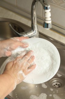 Close-up of a woman washing dishes in the kitchen sink with a scouring sponge full of soap and soap