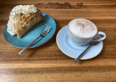 Cup of cappuccino, teaspoon and piece of apple pie with whipped cream on plate, cake fork, wooden