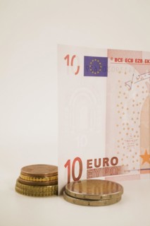 Close-up of 10 Euro bank note and piles of assorted gold and copper colored coins on white