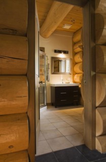 Wooden vanity with white rectangular sink in illuminated guest bathroom with tan ceramic tile floor