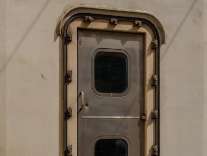Close-up of a metallic train door with a small window and rivets, in South Korea
