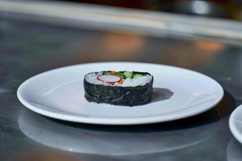 A piece of sushi with rice and cucumber wrapped in seaweed on a plain white plate, AI generated