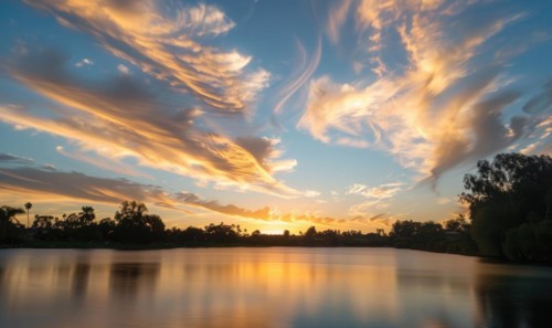 The sun peeking through a fluffy cumulus clouds, clouds reflected in water surface, sunset on the