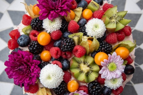 Delicious-looking cake garnished with a variety of berries and colourful flowers on a patterned