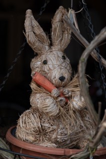 Straw wicker rabbit with carrot, sitting in front of a dark background as an Easter decoration,