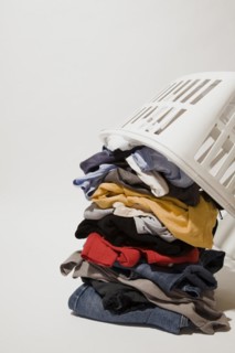 Close-up of white plastic laundry hamper or basket on top of pile of dirty clothes that includes