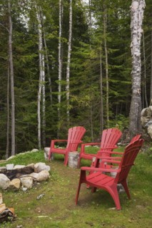 Four bright red plastic Adirondack chairs around rock edged firepit dug into the ground in backyard