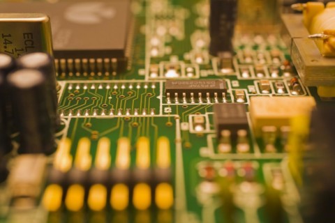 Close-up of green and golden lighted yellow electronic computer circuit board with capacitors,