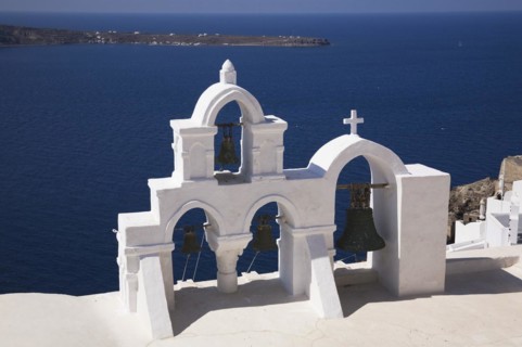 White roughcast cladded arched church bells tower with cross overlooking the Aegean sea, Oia