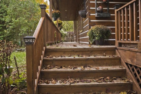 Old and worn brown stained wooden stairs and long veranda with pine wood rocking chair and fallen