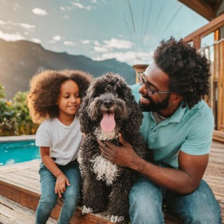 A man and a little girl are posing with a dog. The dog is wagging its tail and the girl is smiling.